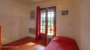 Een slaapkamer met een bed, een raam met gordijnen, een radiator en een klein tafeltje met een lamp.