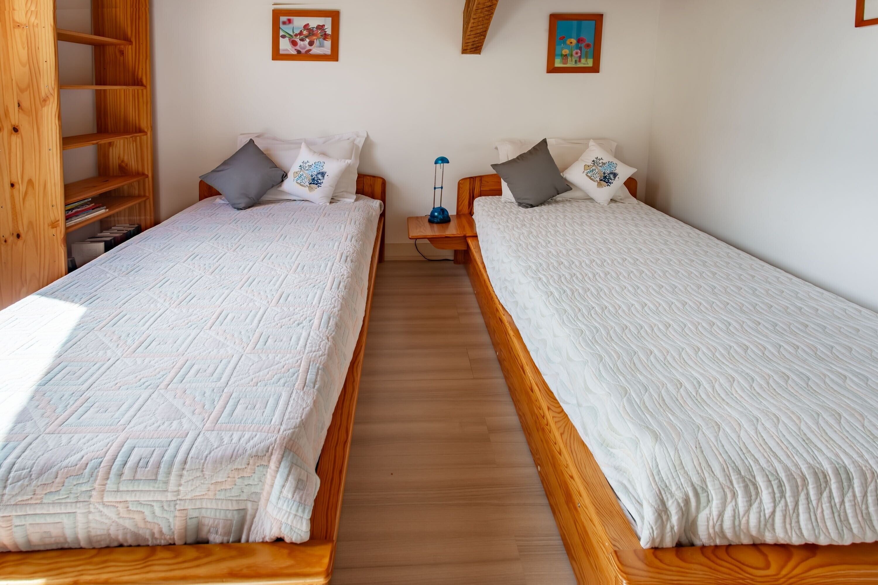 Una habitación con dos camas de madera, una mesita de noche con una lámpara y una estantería de madera.