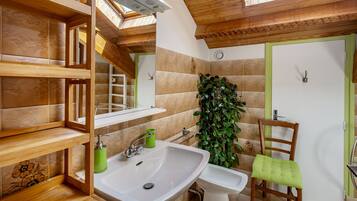 A bathroom with a wooden ceiling, a sink, a bidet, a chair, and a green plant.