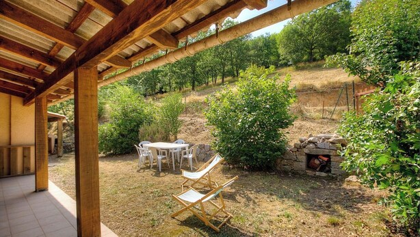 Un espacio al aire libre cubierto con una mesa y sillas, rodeado de follaje y una estructura de piedra.