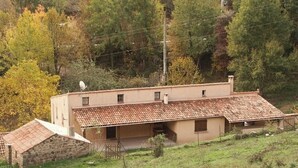Un edificio de dos pisos con techo de tejas, una antena parabólica y una estructura de piedra a la izquierda.