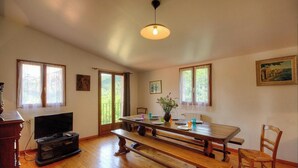 Amplia habitación con una mesa de madera para comer, un televisor y un ventanal con vistas a la vegetación.
