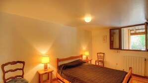 Un dormitorio con una cama, dos lámparas de noche, una silla, un ventanal y un radiador.