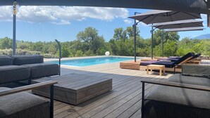 Eine Holzterrasse mit Pool, Liegestühlen und Sonnenschirmen.