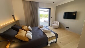 Ein modernes Hotelzimmer mit Bett, Sessel, Fernseher und Blick durch ein großes Fenster.