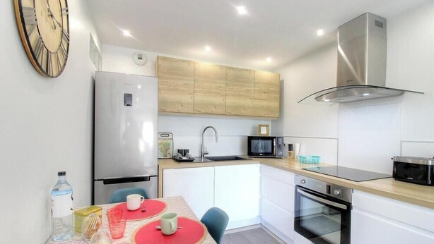 Een kleine keuken met een koelkast, magnetron, oven en een klok aan de muur.