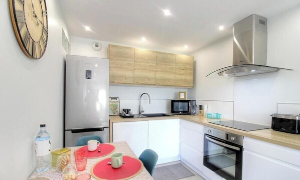 A compact kitchen with a refrigerator, microwave, oven, and a clock on the wall. - Le 28081 - ALATA - Gîte (ALATA)