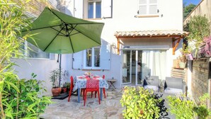 Een terras met een tafel, stoelen, een groene parasol en potplanten.