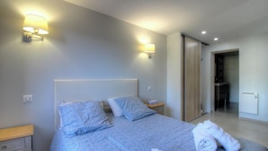 Een slaapkamer met een bed, twee nachtkastjes, een wandlamp en een schuifdeur naar een badkamer.