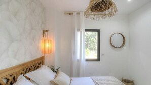 Ein Schlafzimmer mit einem Bett, einer Wandlampe, einem Fenster und einem runden Spiegel.