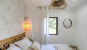 Ein Schlafzimmer mit einem Bett, einer Wandlampe, einem Fenster und einem runden Spiegel.