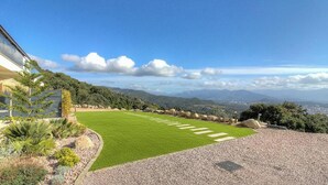 Ein angelegter Garten mit Rasen, Kiesweg und Blick auf ferne Berge.