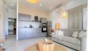 Ein modernes Wohnzimmer mit grauem Sofa, einem runden Couchtisch und einer Küchenzeile mit grauen Schränken und Geräten.
