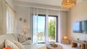 Ein modernes Wohnzimmer mit einer Couch, einem runden Couchtisch, einem Fernseher und einem Balkon mit Gartenmöbeln.