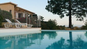 Una piscina con una casa e poltrone relax sullo sfondo.