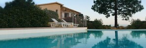 Ein Schwimmbecken mit einem Haus und Liegestühlen im Hintergrund.