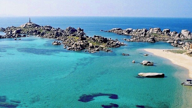 Paesaggio costiero con formazioni rocciose, acqua cristallina e una barca sulla spiaggia.