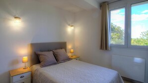 Un dormitorio con cama, dos lámparas de noche, una ventana con cortinas y un radiador.