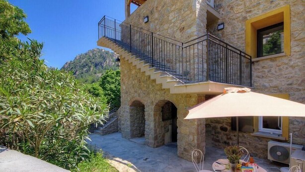 A stone building with a balcony, outdoor seating, and a view of the surrounding landscape. - U Furconi - CHISA - Gîte (CHISA)