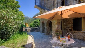 A stone building with a balcony, outdoor seating, and a view of greenery and mountains. - U Furconi - CHISA - Gîte (CHISA)