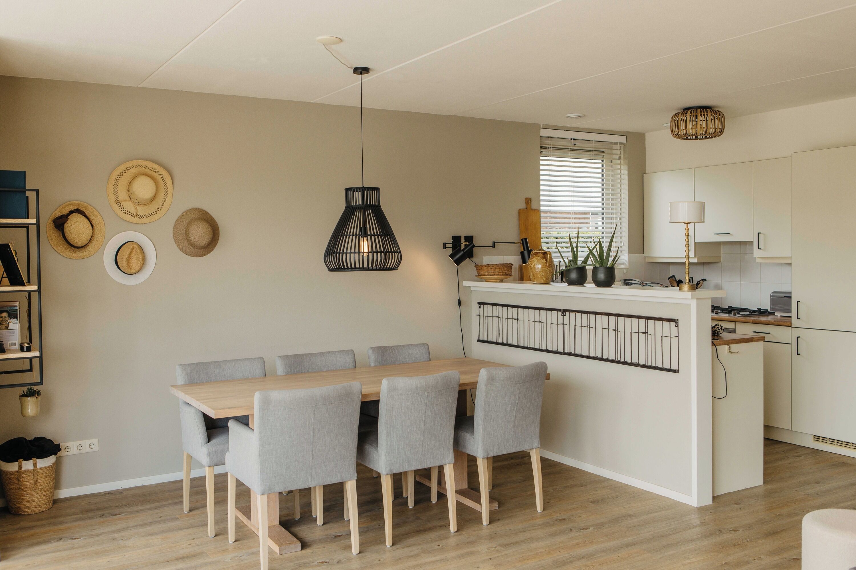 Una cocina moderna con una isla central, una zona de comedor con una mesa de madera y sillas grises, y una lámpara colgante.