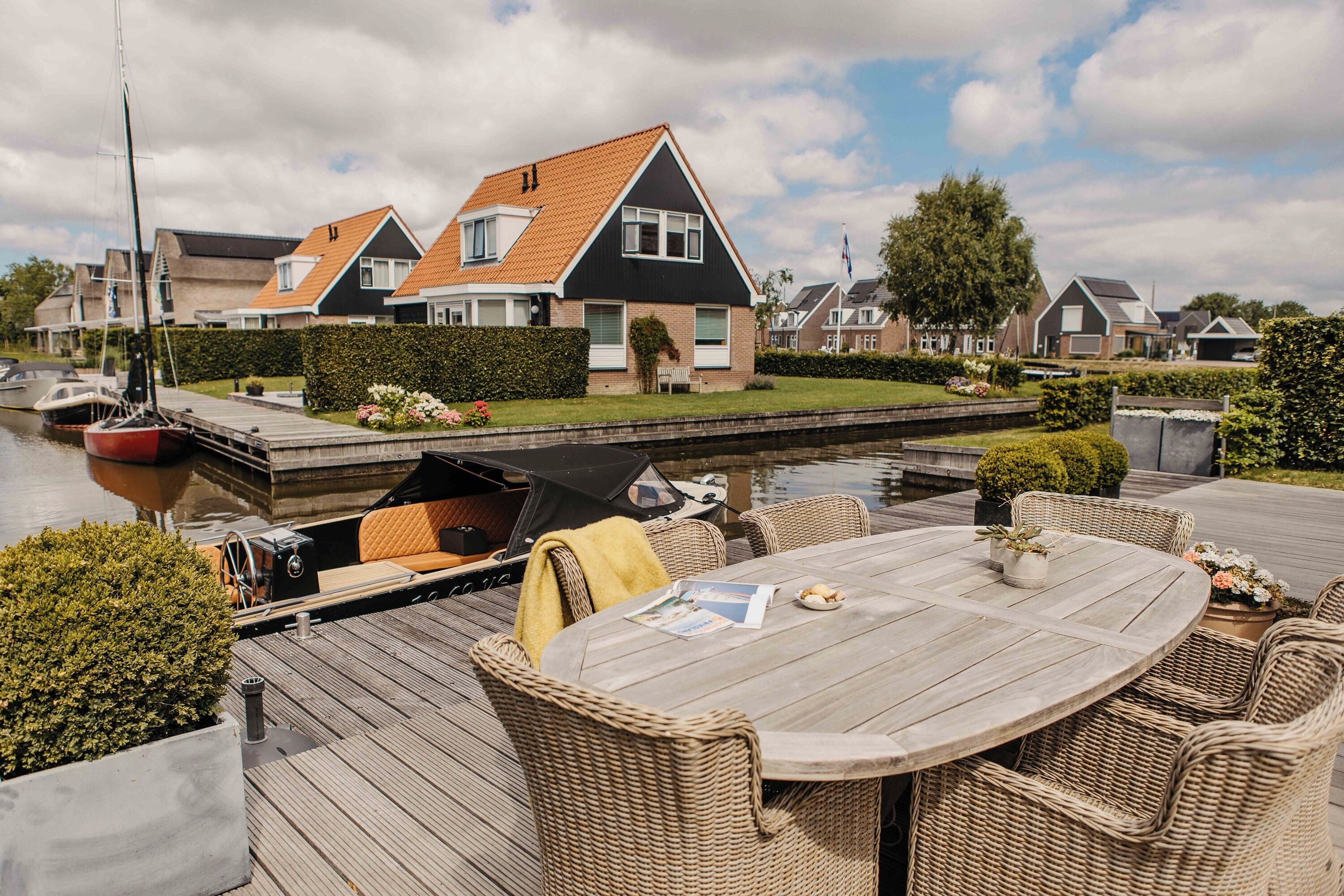 A wooden deck with wicker furniture, a covered area, and a canal view.