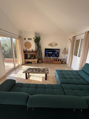 Amplia sala de estar con un televisor grande, sofás verdes, una mesa de centro y una planta en maceta.
