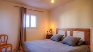 Une chambre à coucher avec un lit, une chaise, une table de chevet avec une lampe et une fenêtre avec des rideaux.