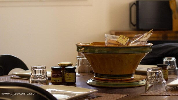 Une table à manger avec un grand saladier en céramique, des pots à condiments et un verre.
