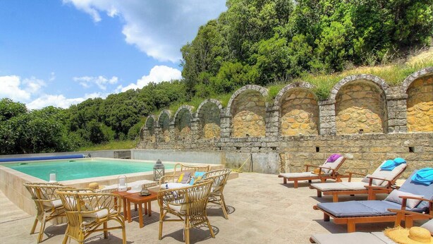 Uma área à beira da piscina com arcos de pedra, mobiliário de vime e espreguiçadeiras.