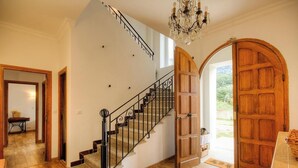 Uma escadaria com corrimão preto, uma porta de madeira e um candelabro.