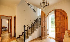 A staircase with a black railing, a wooden door, and a chandelier. - Fraschella - MOCA CROCE (MOCA CROCE)