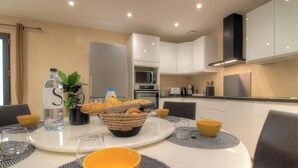 Una cocina moderna con armarios blancos, una mesa de comedor servida con platos, vasos y una cesta de pan.