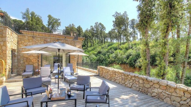 Una terraza con mobiliario exterior, paredes de piedra y vista a árboles.