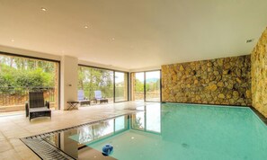 Ein modernes Hallenbad mit Steinwänden, großen Fenstern und einer Sitzecke mit Stühlen.