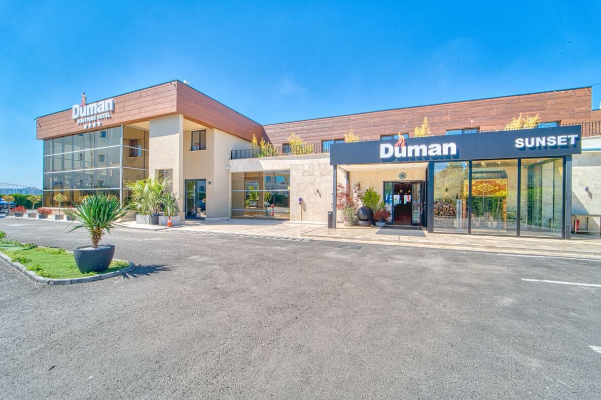 Un hotel Duman de diseño moderno, con una entrada destacada y un área exterior visible con plantas en macetas.