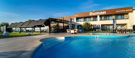 A hotel with a pool, outdoor seating, and a covered area.