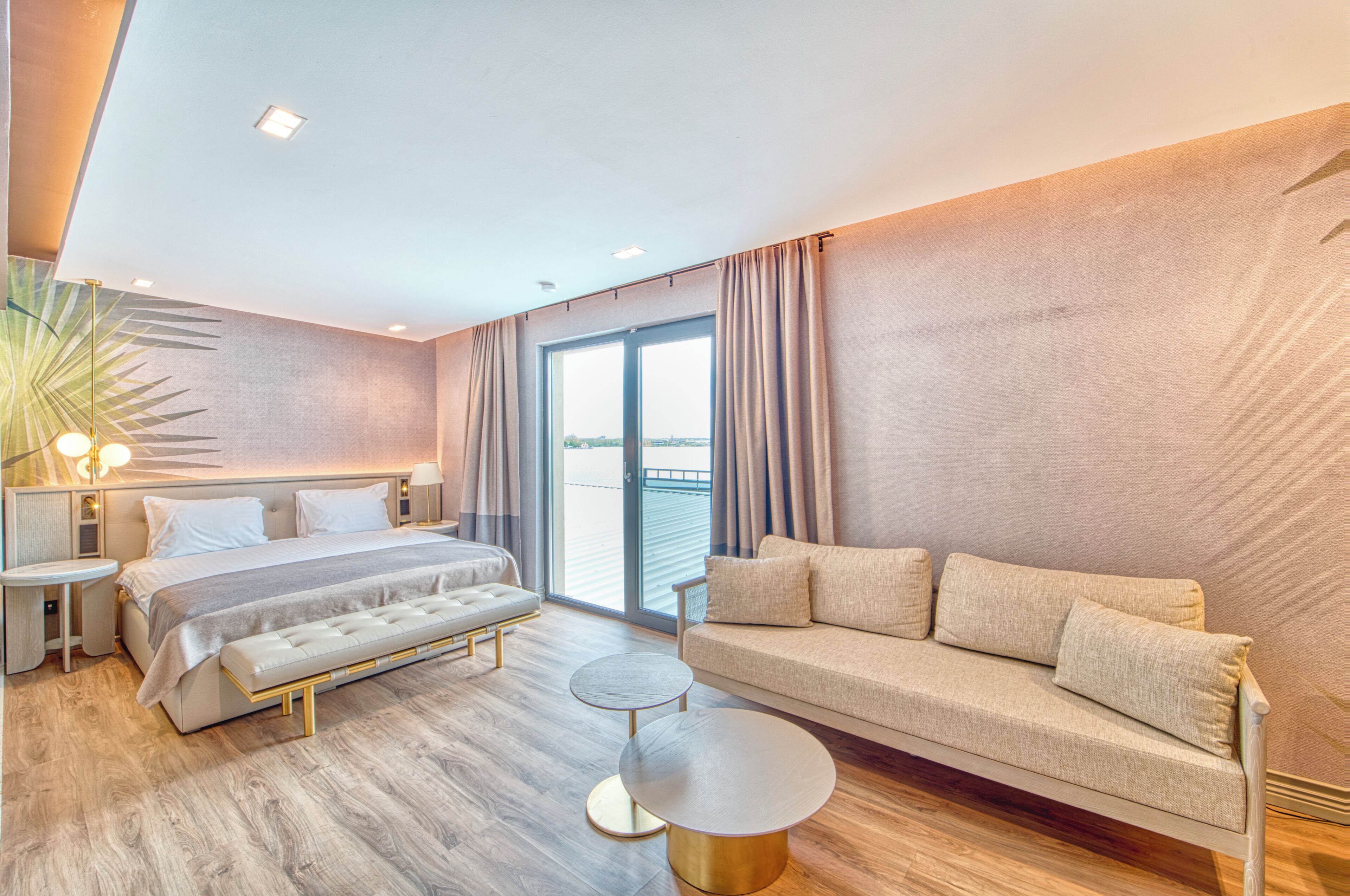 Ein modernes Hotelzimmer mit Bett, Sofa, Nachttischen und Balkonblick.