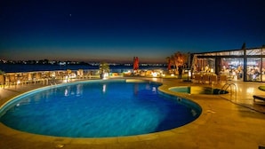 Piscina con vistas al mar por la noche, mobiliario exterior y un restaurante.