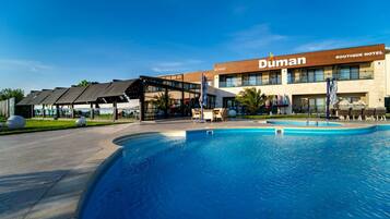 A hotel with a pool, outdoor seating, and a covered area.
