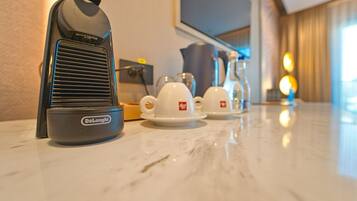 Un calentador portátil DeLonghi sobre una encimera de mármol, con dos tazas y platillos blancos al fondo.