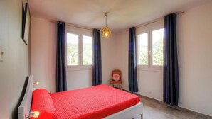 Quarto com cama, duas janelas, uma cadeira e luminária pendente.
