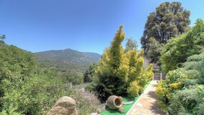 Um jardim com um caminho, uma rocha grande e vista para montanhas.