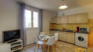 Cozinha compacta com área de refeições, máquina de lavar e televisão.