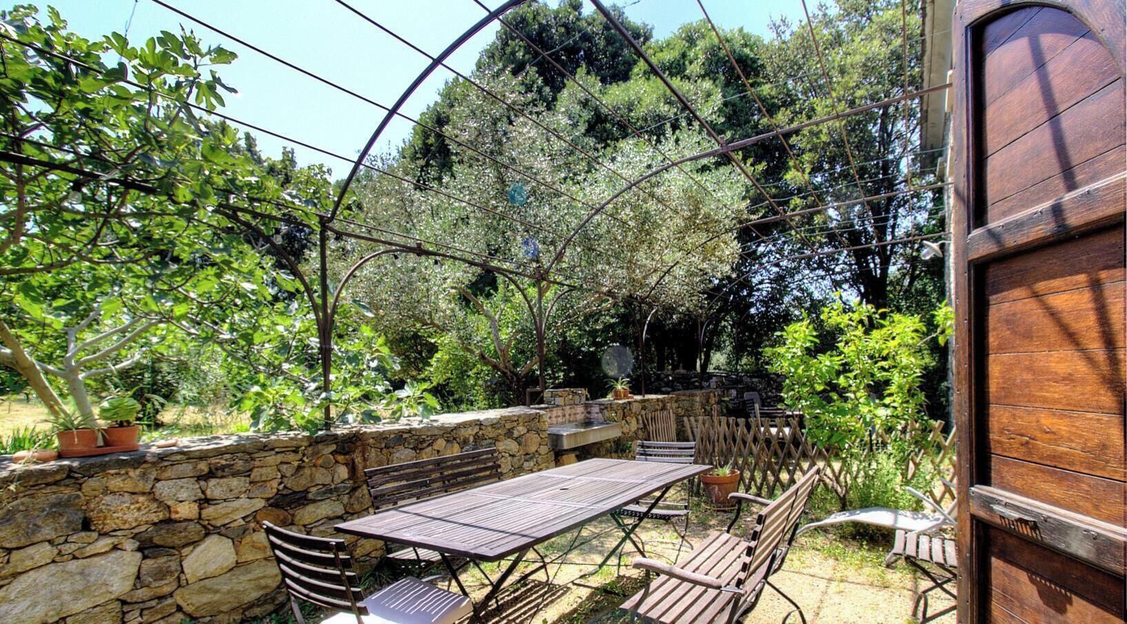 Un patio esterno con un muro in pietra, un tavolo di legno e sedie in metallo.