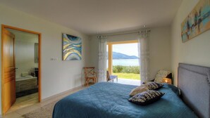 Een slaapkamer met een bed, een stoel, een schilderij, uitzicht op de omgeving en een deur naar de badkamer.