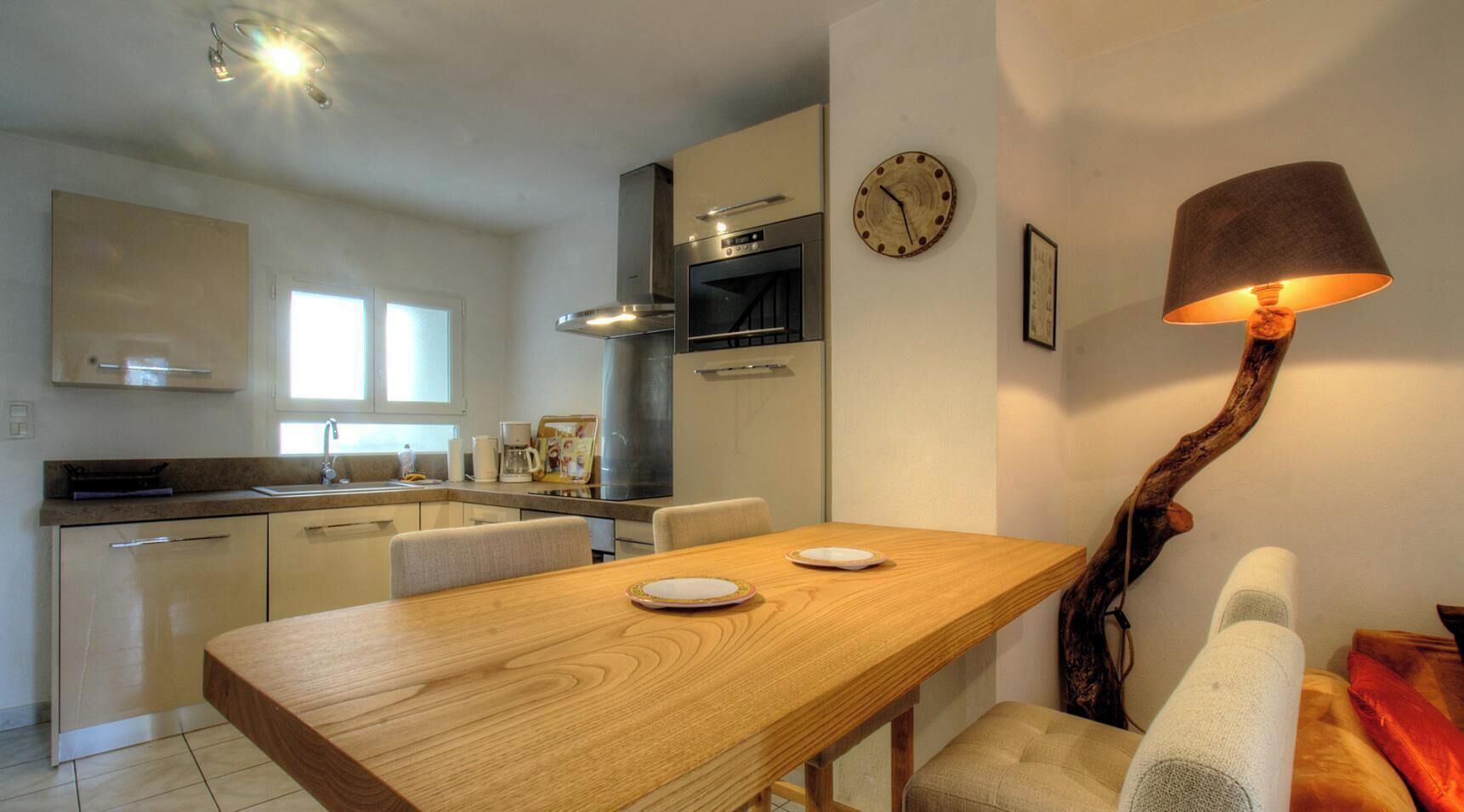 A modern kitchen with a dining table, chairs, a clock, and a unique lamp.