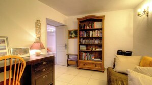 A cozy living room with a wooden bookshelf, a desk with a lamp, a chair, and a sofa. - Casa Paterna - VENACO (VENACO)