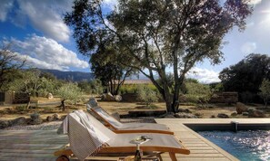 Ein Poolbereich mit Liegestühlen, einer Holzterrasse und Blick auf die umliegende Landschaft.