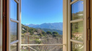 Ein offenes Fenster mit Blick auf eine gebirgige Landschaft und ein Haus.